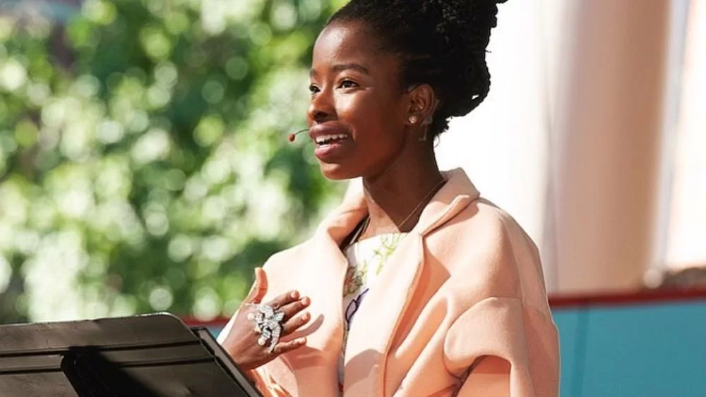 Amanda Gorman on Pink coat speaking with ear phones on her ears