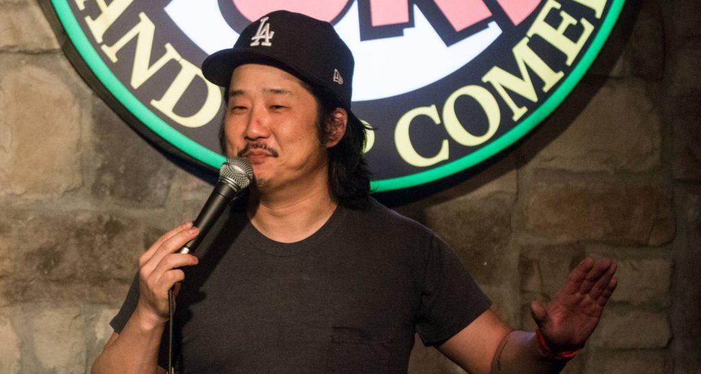 Bobby Lee on black face cap holding a microphone