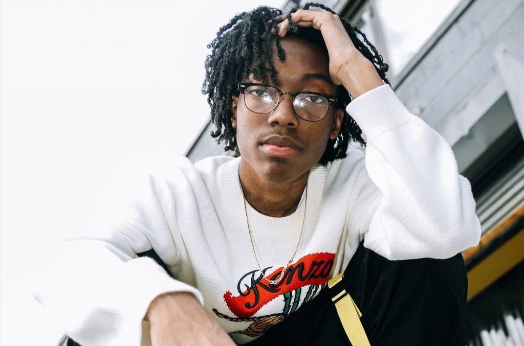 Lil Tecca wearing glasses and squatting down