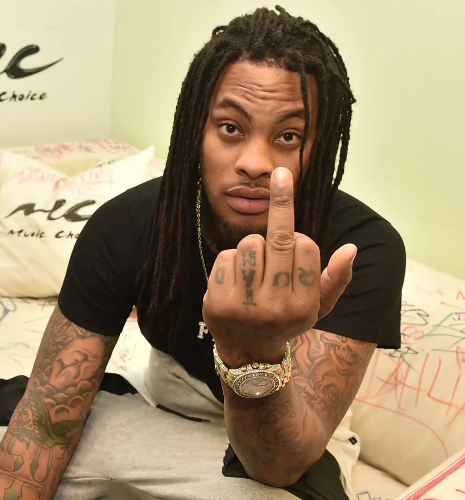 waka flocka wearing a black top and sitting on the bed