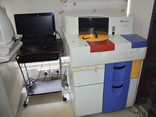 A black computer system on a table beside a clinical chemistry autoanalyzer