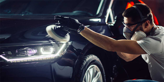 a worker on nose protector applying Teflon coating to wash a black car