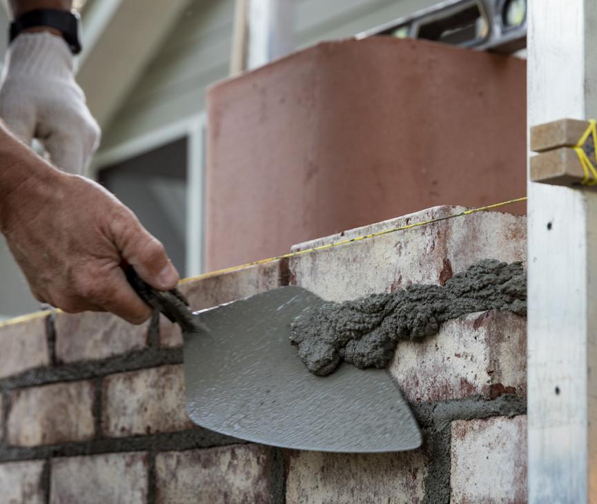 worker using trowel to lay cement mortar on bricks 