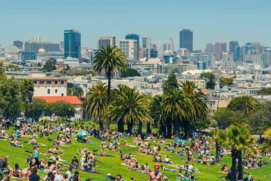 lot of people sitting on the ground in a large public park with trees